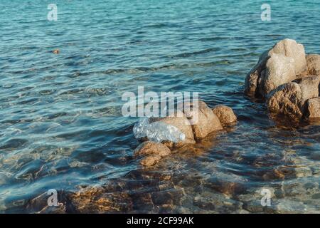 Empty plastic crumpled bottles waste lying in clear water on seaside near rocks Stock Photo