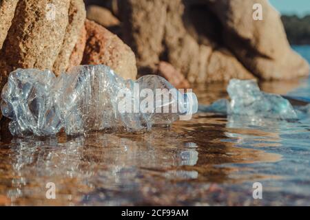 Empty plastic crumpled bottles waste lying in clear water on seaside near rocks Stock Photo