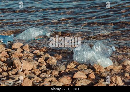 Empty plastic crumpled bottles waste lying on the seaside rock near clear water Stock Photo