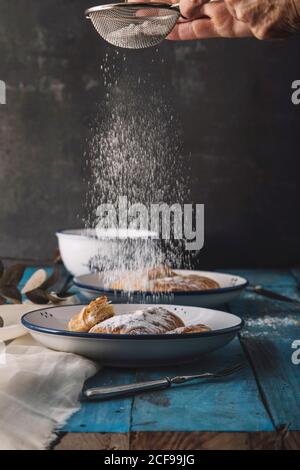 unrecognizable chef putting powdered sugar on dessert while cooking delicious buns on blue table Stock Photo