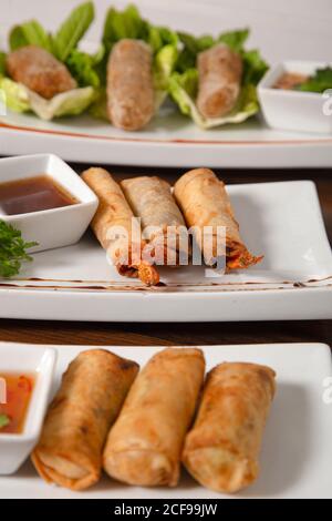 Traditional Asian crispy fried spring rolls with various fillings served with sauces and green salad Stock Photo