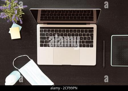 From above of laptop placed on black table near protective mask and bottle of antiseptic Stock Photo
