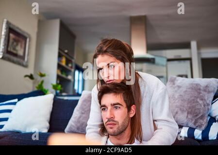 Positive young Woman hugging happy man while sitting on sofa in cozy living room Stock Photo