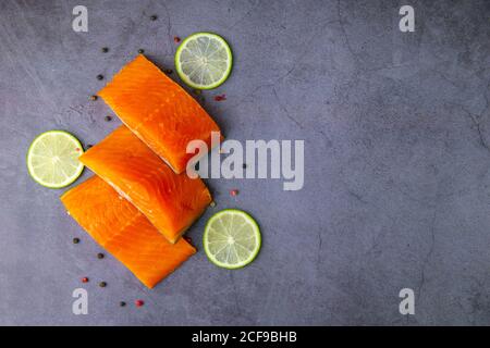 Three pieces of raw salmon with spices and lemon on a grey background. Spiced healthy salmon filets uncooked Stock Photo