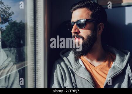Thoughtful young bearded man looking through window while traveling by train Stock Photo