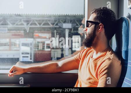 Thoughtful young bearded man looking through window while traveling by train Stock Photo