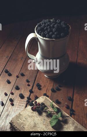 Vintage jag with ripe blackberries on wood and leaves on a old book Stock Photo