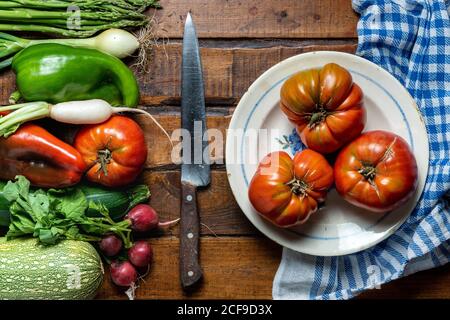 Fresh organic vegetables on a dark wooden table with tomatoes in a bowl and a knife Stock Photo