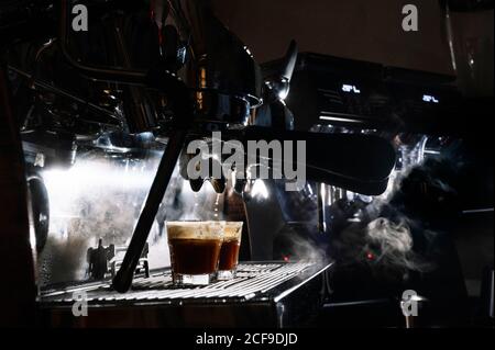Glasses with hot coffee placed on metal panel of professional coffee maker in dark cafe Stock Photo