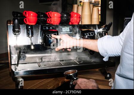 faceless male barista standing with portafilter in coffee shop and using professional coffee machine for preparing delicious drink Stock Photo