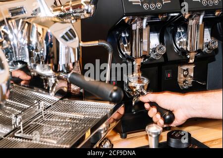 Male barista holding coffee in portafilter while making fresh beverage in professional coffee machine Stock Photo