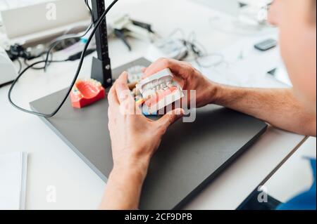 From above crop male student hands holding denture and paste while sitting at table during dentistry class Stock Photo