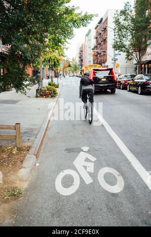 Back view of faceless sportsman riding bicycle on cycle lane amid city street with green plants Stock Photo