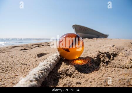 Orange glass ball on sand near the sea. Abstract conceptual photo. Stock Photo