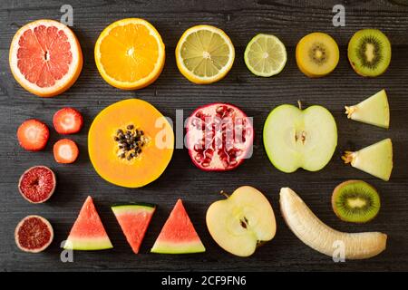 Top view of various peeled and cut healthy fruits and vegetables arranged on black lumber table Stock Photo