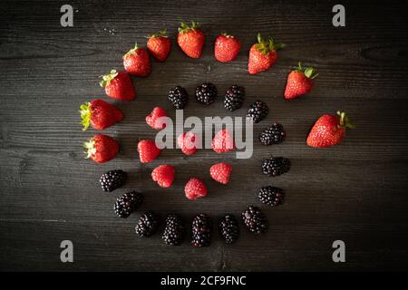 From above bunch of assorted ripe berries arranged in spiral on dark wooden table Stock Photo