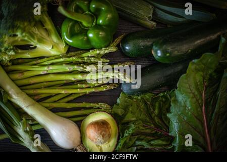 Bunch of various green vegetables placed on dark wooden table on black background Stock Photo