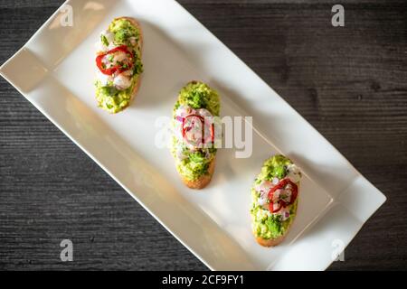 From above top view of delicious small sandwiches with shrimp and vegetables placed on ceramic plate on black table in cafe Stock Photo