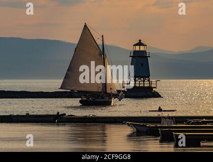 a sloop sailing by the lighthouse on the waterfront of Lake Champlain in Burlington, Vermont Stock Photo