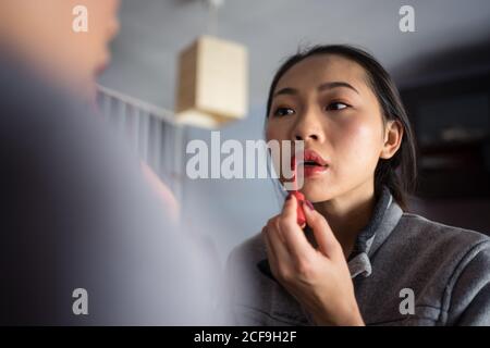 Young Woman applying lipstick in front of mirror Stock Photo