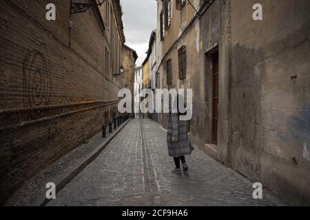 Woman walking on aged empty alleyway with old buildings Stock Photo