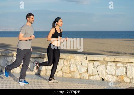 Healthy content couple in sports clothing smiling while jogging by the ocean side coast on blurred background Stock Photo