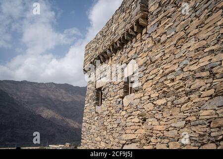 Exterior of ancient stone wall of historic building of Marble Village in Al Bahah against background of rocky terrain and cloudy sky in summer in Saudi Arabia Stock Photo