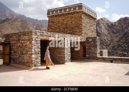 monumental ancient building with remote female tourist coming out of doorway in yellow dress while enjoying hot sunny day in Marble Village in Al Bahah Stock Photo