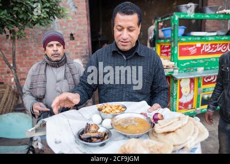 Cairo, Egypt - December 14, 2019: Ethnic male with carrying tray with various dishes serving clients in street cafe Stock Photo