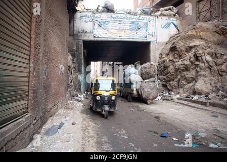 Cairo, Egypt - December 14, 2019: Tuk tuk car driving down empty road with garbage and decayed buildings Stock Photo