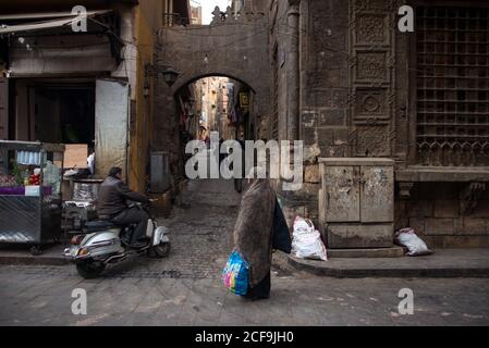 Cairo, Egypt - December 14, 2019: Male driving on scooter down aged narrow street with cobblestone pavement and with antique buildings Stock Photo