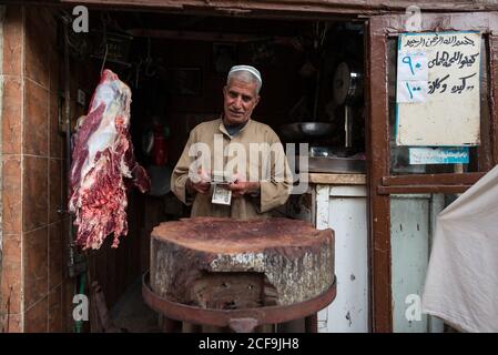 Cairo, Egypt - December 14, 2019: Ethnic man in uniform counting money in market stall looking at camera Stock Photo