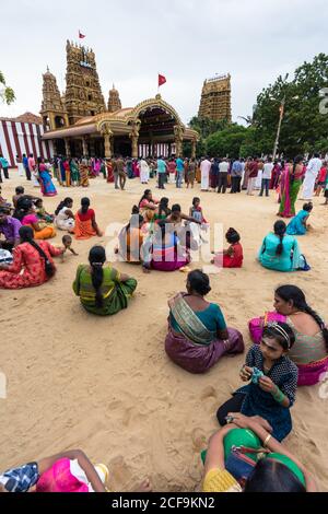 Jaffna, Sri Lanka - August, 9 2019: Happy Tamil kids smiling and looking at camera while sitting on sand near woman in traditional clothes during Nallur Kandaswamy Kovil Festival Stock Photo