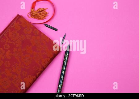 View on isolated notebook with red floral pattern cover, old feather ink pen and bookmark on pink background with copy space for text Stock Photo