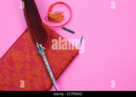 View on isolated notebook with red floral pattern cover, old feather ink pen and bookmark on pink background with copy space for text Stock Photo