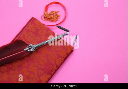 View on isolated notebook with red floral pattern cover, old feather ink pen and bookmark on pink background with copy space for text Stock Photo