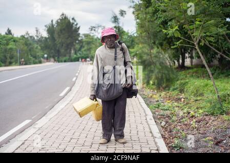 Ruanda, Africa - December 14, 2019: Homeless African American male with bags strolling on road of city looking at camera Stock Photo