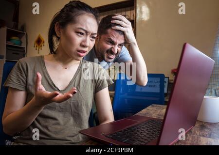Low angle of multiethnic couple having problems with computer while working together on project online Stock Photo