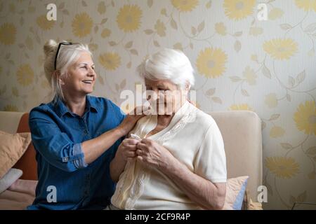 Woman helping senior woman dress in her bedroom Stock Photo