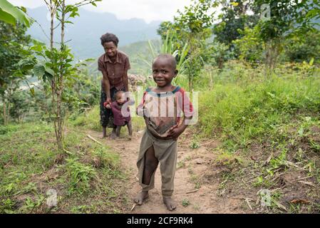 Uganda - November, 26 2016: Bald African toddler looking at camera while walking on dirty road outside village Stock Photo