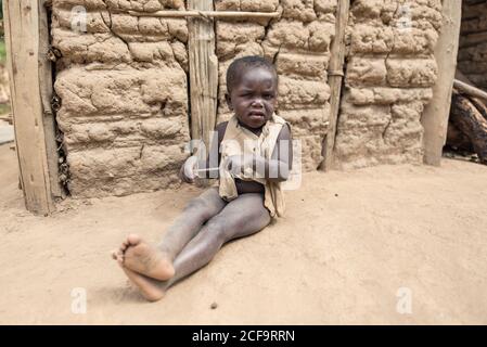 Uganda - November, 26 2016: African sad girl crying looking at camera while sitting on dirty road outside village Stock Photo