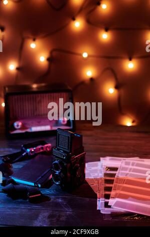 Black retro photo camera with notebook and film composed with vintage radio on wooden table in garland light Stock Photo