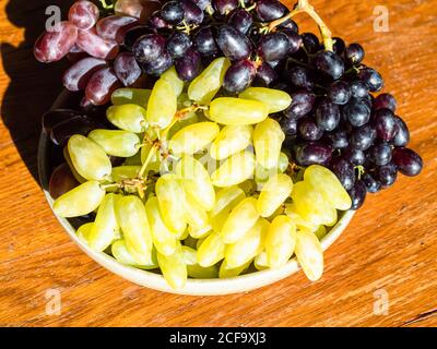 bunches of crimean white ladyfinger and red seedless grapes on plate on wooden table illuminated by evening sun Stock Photo