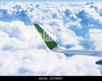 airplane wing over white cumulus clouds in blue sky during flight on summer day Stock Photo