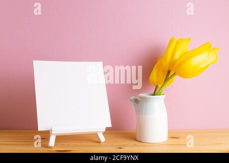 Blank canvas on easel with yellow tulip flowers on wooden table with pink background Stock Photo