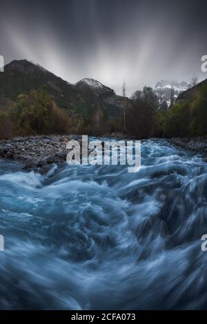 Picturesque scenery of narrow creek with stony shore flowing among forest in winter Stock Photo