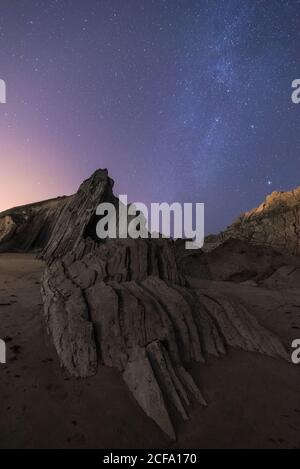 From below of rough cliff peak with colorful blue night sky and shiny stars on background Stock Photo