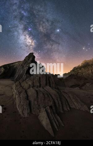 From below of rough cliff peak under milky way colorful blue night sky and shiny stars on background Stock Photo