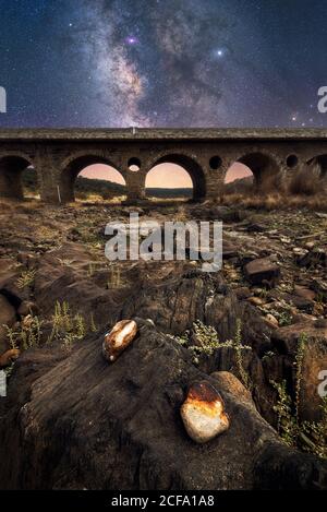 Rocky ground and old stone bridge with colorful night sky with milky way and stars on background Stock Photo