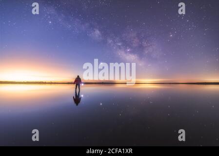 Silhouette of anonymous man standing on reflection surface of water and reaching out to starry colorful night sky with milky way Stock Photo